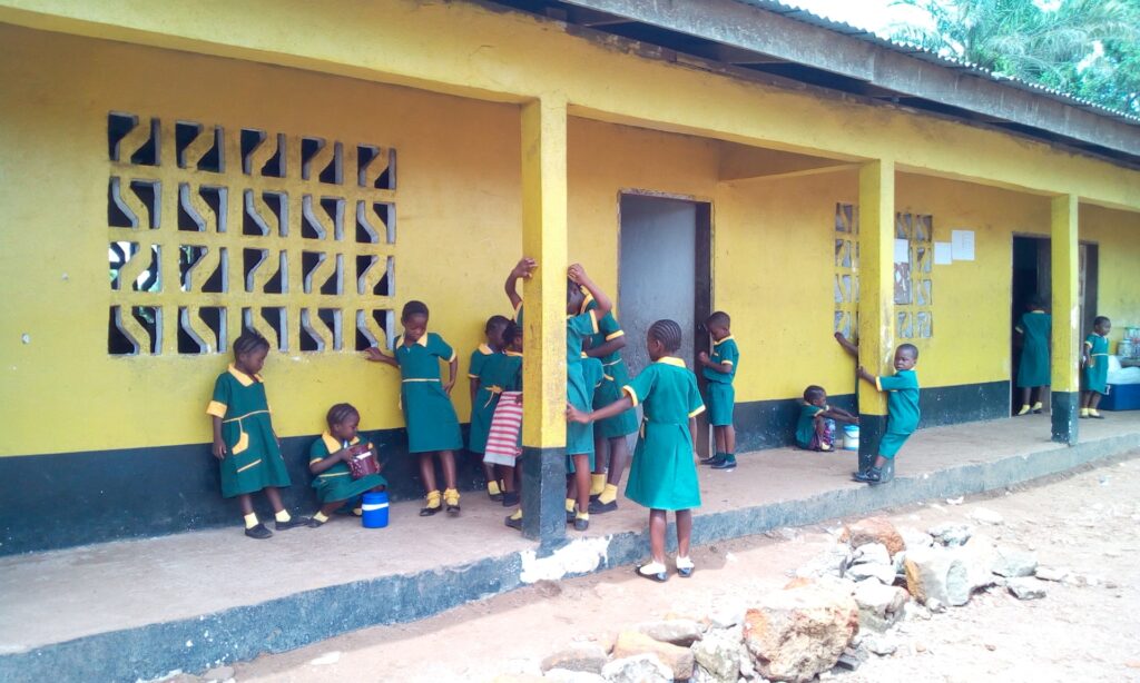 students in Liberia outside a yellow school building